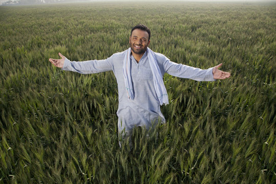 Portrait of an Indian man standing with arms out in a field 