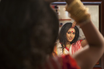 Fototapeta na wymiar Bengali woman putting sindoor on her forehead