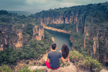 Couple on a rock overlooking a canyon with a river on the bottom and rocky walls covered by green trees.  Retro color tones. Furnas Canyon is a common tourist destination in Brazil