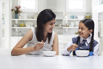 Mother and daughter at table eating breakfast 