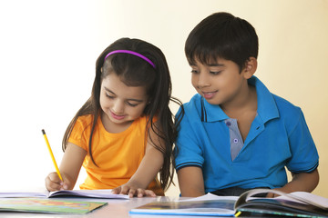 Smiling children studying at table against colored background