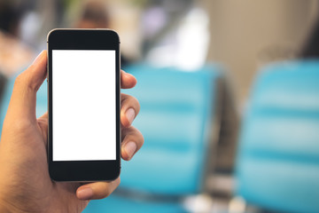 Mockup image of a man's hand holding black mobile phone with blank white screen in airport background