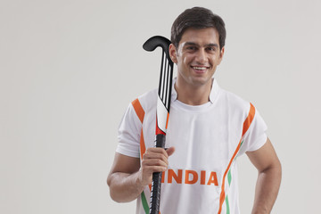 Portrait of confident young man holding hockey stick isolated over gray background