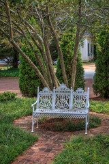 Classic white iron outdoor settee furniture sitting in front of a tree on a circular walkway.