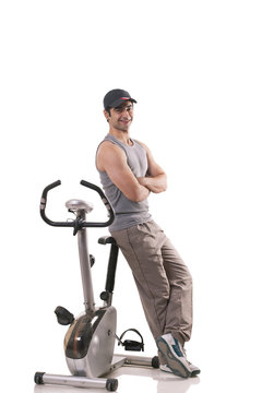 Portrait of a young man with arms crossed leaning on exercise bike over white background 