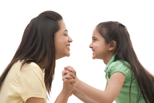 Side view of cheerful mother and daughter holding hands over white background 
