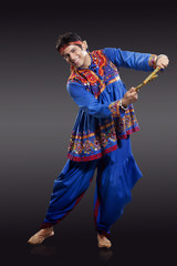 Full length portrait of young man in traditional wear performing Dandiya Raas isolated over black background