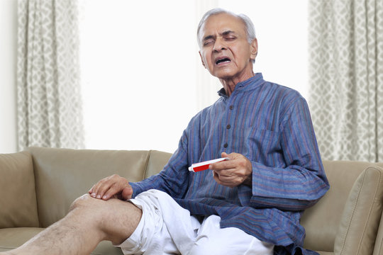 Elderly man applying ointment on knee 