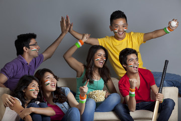 Excited young friends enjoying cricket match together at home