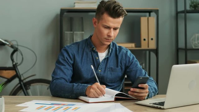 Young business man using smart phone fot noting something in the note book while working in the office.
