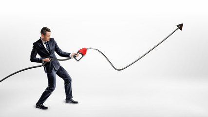 A businessman holds a gas pump nozzle which shots out oil into a black raising line with an upwards...