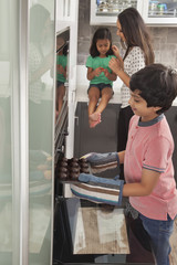 Boy baking cup cakes into oven with family