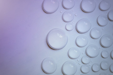 Big and small water drops on purple background. Closeup.