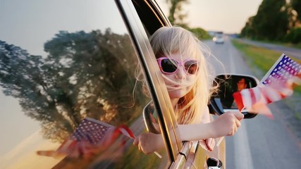 A 6 year old girl with an American flag looks out the window of a moving car
