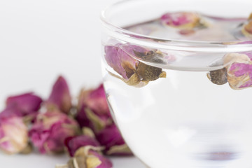 A cup of rose tea with dried rose flower on white background.