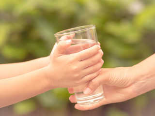 Closeup vintage woman hand giving glass of fresh water to child in the park.  Drink and health care concept.