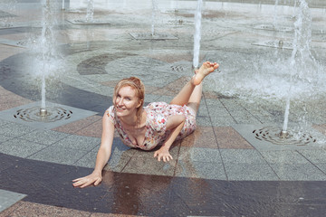 Beautiful wet woman lies in a fountain, she is smiling and happy. Summer is a hot day.