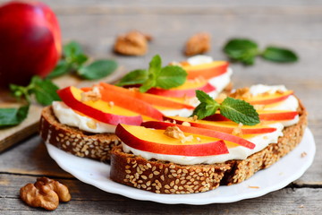 Easy sandwiches with cream cheese, fresh nectarines, walnuts and mint on a plate and on a vintage wooden table. Cream cheese sandwich recipe for kids. Rustic style. Closeup 