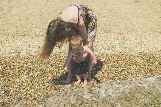 Young mother helping baby go paddle in the sea