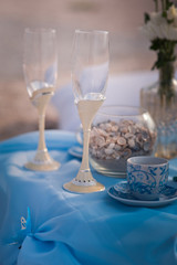 Summer wedding decor in blue. Maritime wedding style. Flowers, beads, table, glasses of champagne, a frame for photos, jars on the background of the sea.