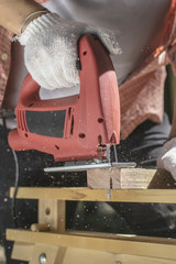 Wood worker cutting wooden panel with jig saw.