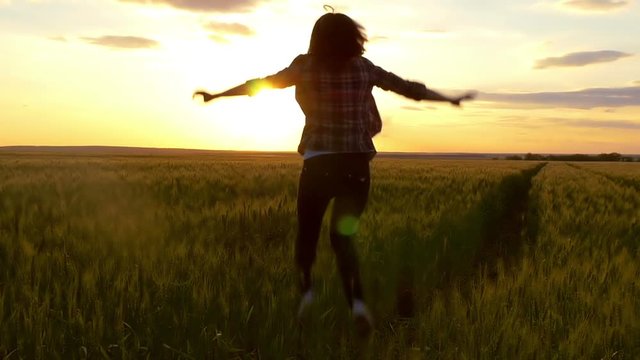 Beauty girl jumping on a yellow wheat field over a sunset sky.