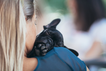 Beautiful young blond woman enjoying with her french bulldog puppy in cafe bar. Close up and...