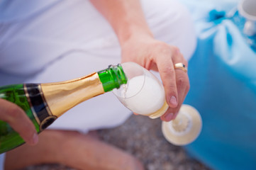 The groom pours champagne into the glass of the bride