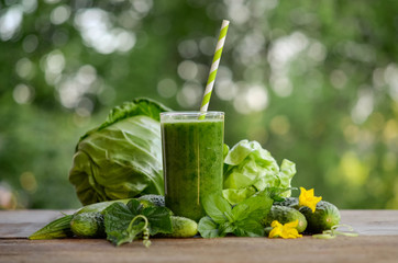  glass with green smoothie on a wooden table and  vegetables with mint leaves