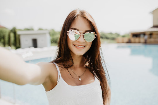 Portrait of beautiful girl taking a selfie at the swimming pool. Summer fun