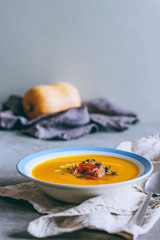 A plate of pumpkin soup with a jamon, garlic, thyme and cream, on a gray background