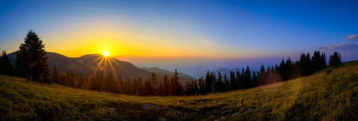 Panorama of a sunrise over a musty mountains and pine forest during late summer