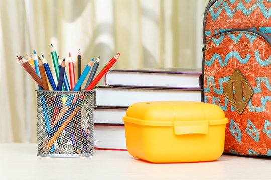 School backpack with school supplies. Books, stand for pencils with color pencils and sandwich box on wooden table