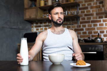 handsome young man pouring milk from bottle at breakfast