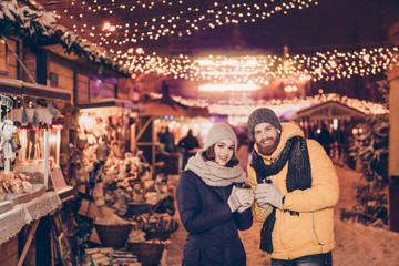 Beautiful young couple outdoors at winter on a new year`s eve with hot drinks, having fun at a...