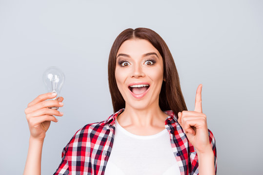 Eureka! Have an idea! Success concept. Young cute female student is standing with a lamp in her hand on pure background in casual outfit