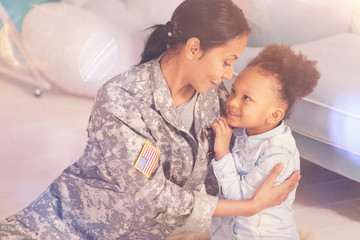 Loving mother in camouflage embracing her petite daughter