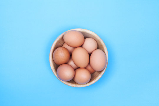 Chicken egg in wood bowl on blue background with space for copy .