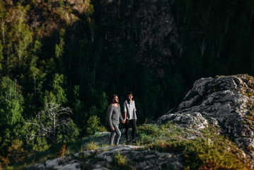 Obraz premium Loving couple at sunset standing on a cliff. A couple in love travels in the mountains. Couple travels. Lovers in nature. Man and woman watching the sunset. Lovers at sunset. Walk in the mountains