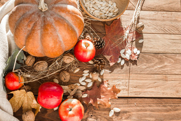 Autumn orange pumpkin, red apples, walnuts, acorns and dry foliage on a wooden background