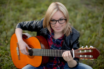 girl sits on the grass with a guitar playing