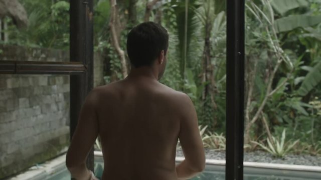 Man stands in the doorway and looks at the pool outside in Bali.