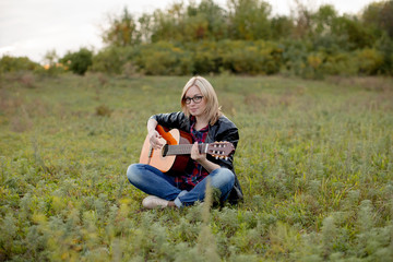  girl sits on the grass with a guitar playing, putting her hands on the strings.