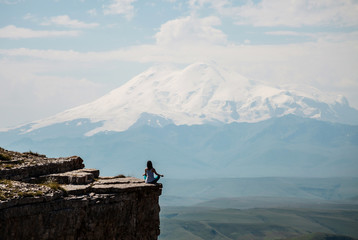 Young woman sitting on the cliff and enjoying view on the Elbrus