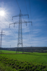 Hochspannungsleitung in saftiger grüner Wiese vor strahlend blauem Himmel mit Sonnenschein, vertikal