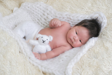 cute asian boy newborn portrait  with white doll one month lie down  on white background fur .