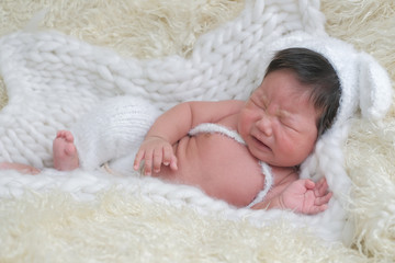 cute asian boy newborn portrait  with white doll one month lie down and cry  on white background fur .
