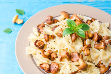 Farfalle pasta with chanterelles and basil on blue wooden table