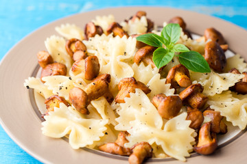 Farfalle pasta with chanterelles and basil on blue wooden table