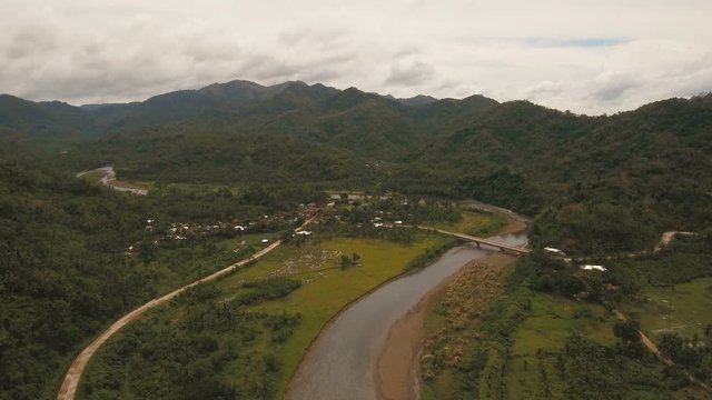 Landscape with lush forest and a river flowing through mossy boulders. Aerial view: Mountain river flows through green forest. Tropical river in the rain forest in Asia. Philippines, Camiguin. 4K